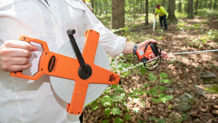 A close-up photo of a measuring devise being used by a student in a wooded setting.