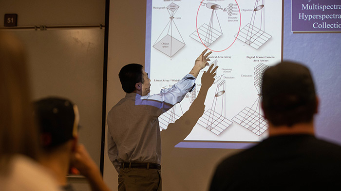 Faculty member, in a classroom, pointing out an important image and/or concept on a large screen.