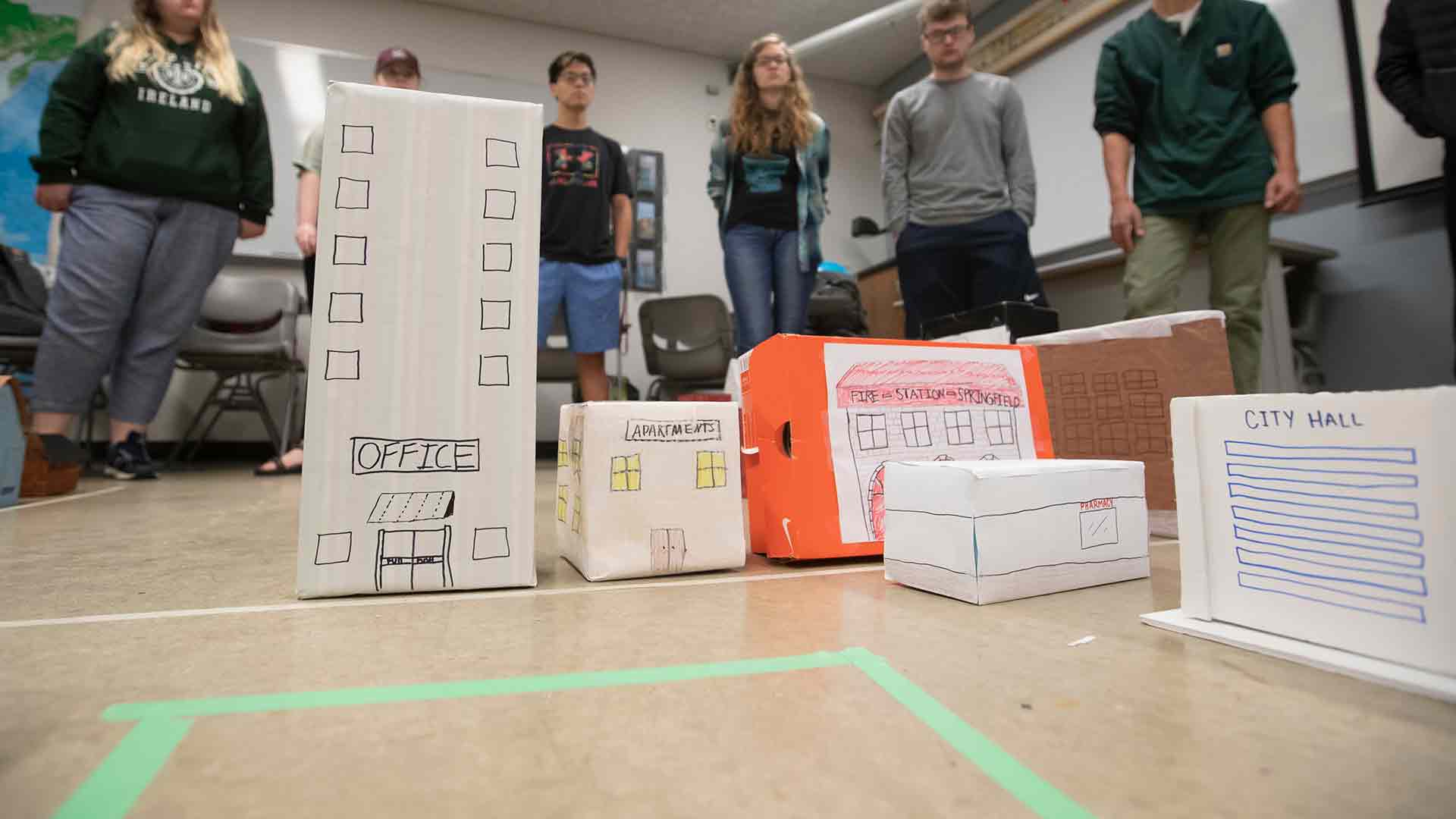 Students standing around a town they created out of small boxes