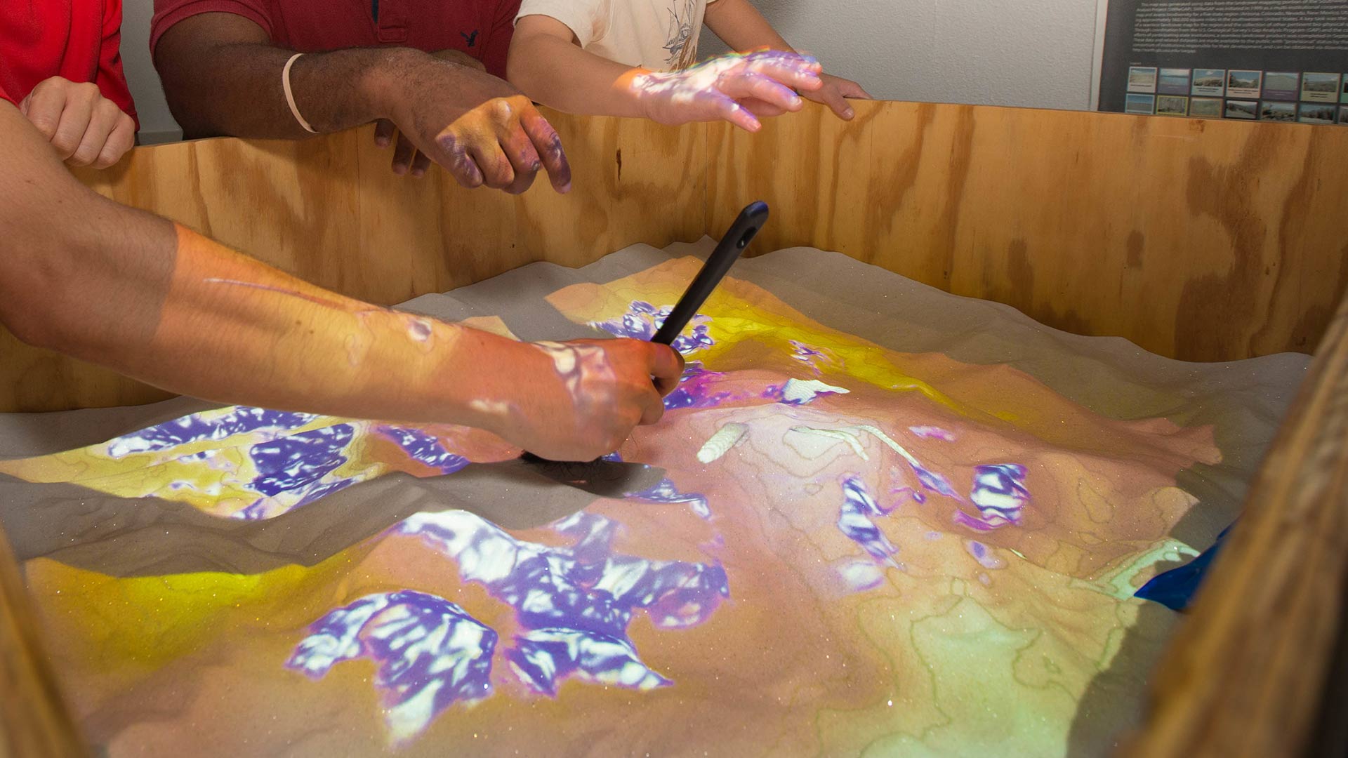 Close up of students working with sand in a wooden box to better understand contours. 