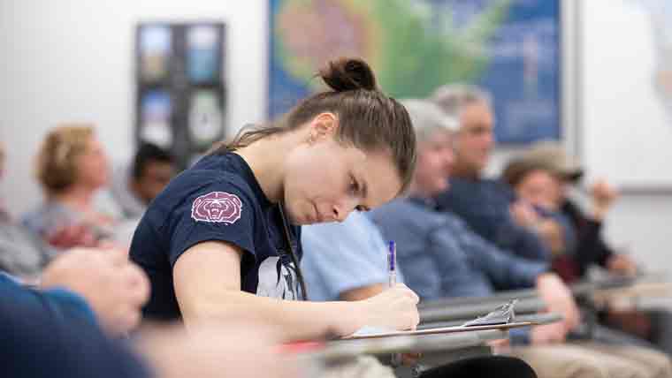 Student concentrating and taking notes in a classroom.