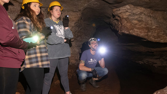 Students on a field trip, underground, in a local cave. They are wearing hard hats and using flashlights to see the cave features.