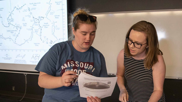 One student communicating about something on a piece of paper to another student.