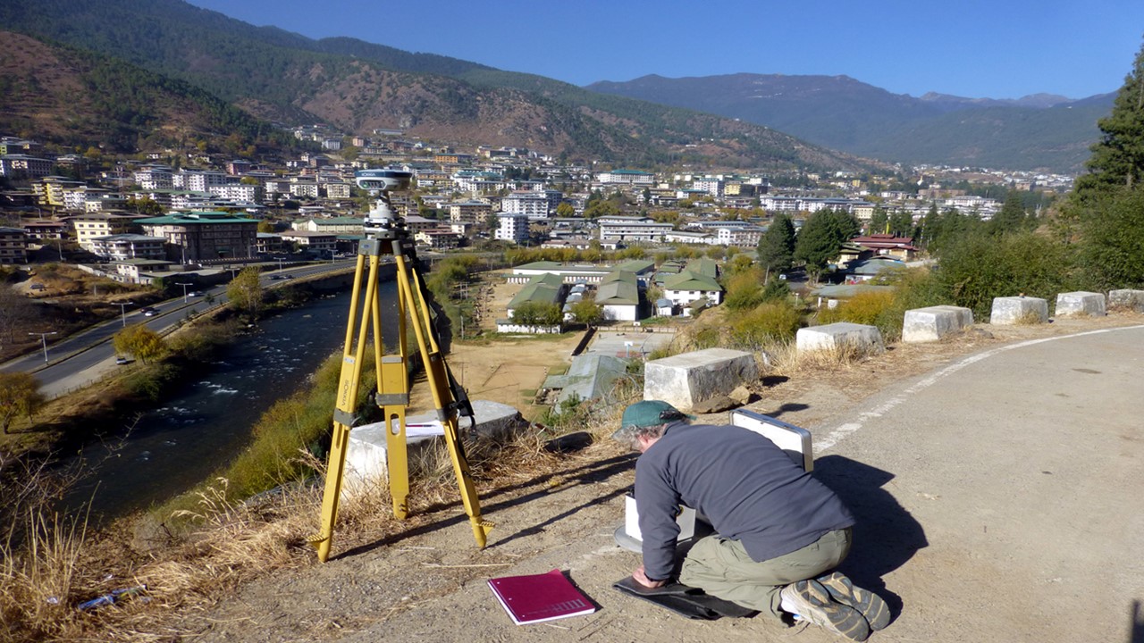 Person kneeling on the ground recording geologic data.