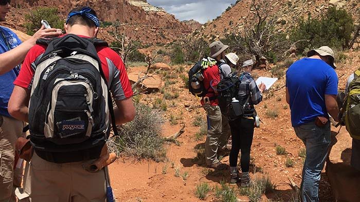 Group of students outdoors and taking notes in a desertlike surrounding.